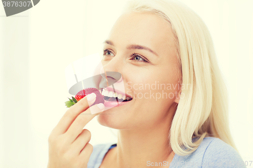 Image of happy woman eating strawberry at home