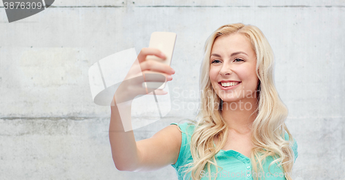 Image of smiling young woman taking selfie with smartphone