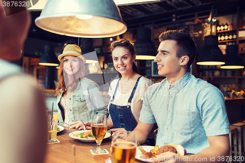 Image of happy friends eating and drinking at bar or pub