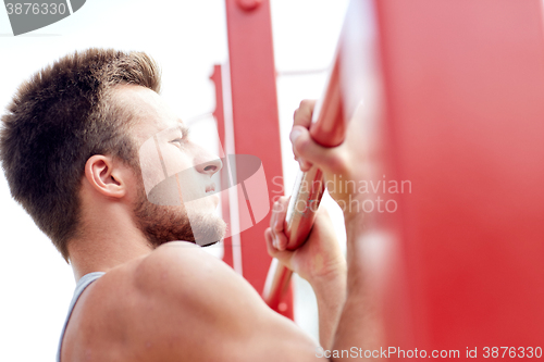 Image of young man exercising on horizontal bar outdoors