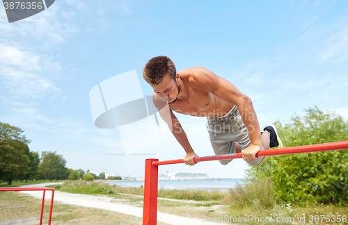 Image of young man exercising on horizontal bar outdoors