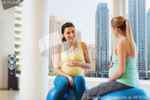 Image of two happy pregnant women sitting on balls in gym