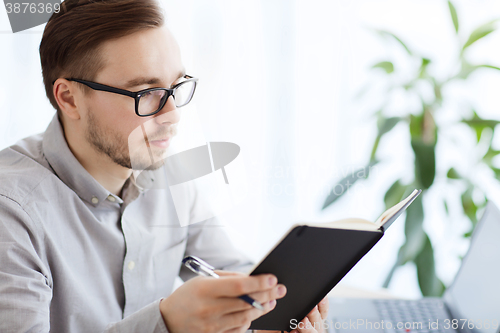 Image of creative male worker with book at home office