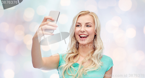 Image of smiling young woman taking selfie with smartphone