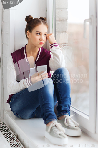Image of teenage girl sitting on windowsill with smartphone
