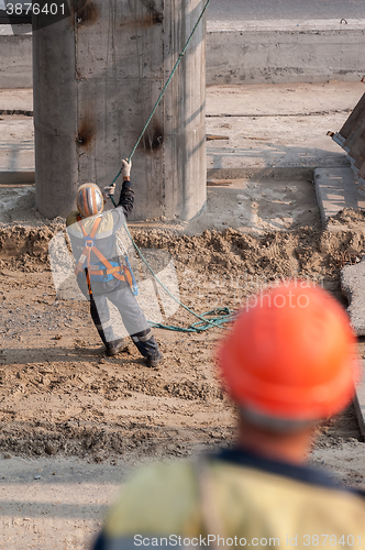 Image of Worker pulls rope to level panel lifted by crane