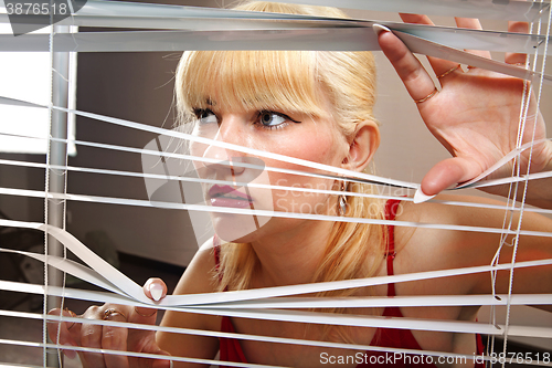 Image of blonde woman observes through blinds