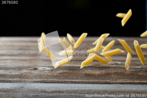 Image of Falling penne pasta. Flying yellow raw macaroni over black background.