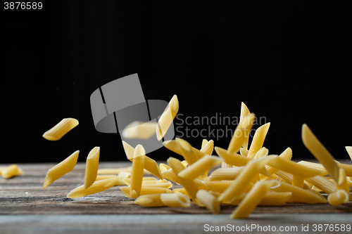 Image of Falling penne pasta. Flying yellow raw macaroni over black background.