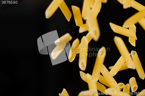 Image of Falling penne pasta. Flying yellow raw macaroni over black background.