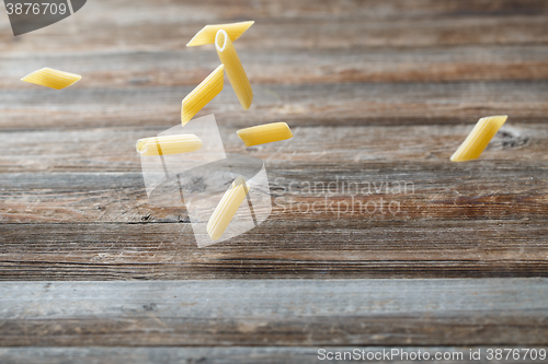 Image of Falling penne pasta. Flying yellow raw macaroni over black background.