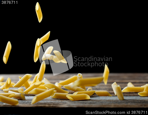 Image of Falling penne pasta. Flying yellow raw macaroni over black background.