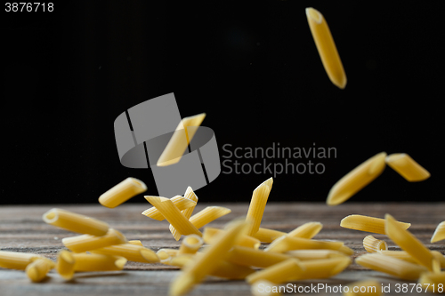 Image of Falling penne pasta. Flying yellow raw macaroni over black background.