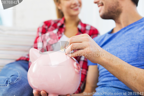 Image of close up of happy couple putting coin to piggybank