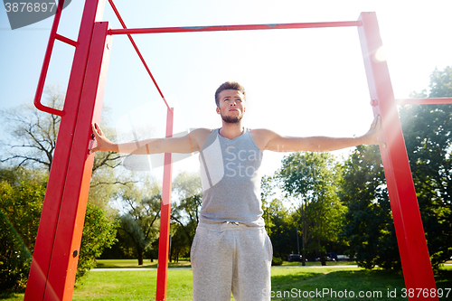 Image of young man exercising on horizontal bar outdoors