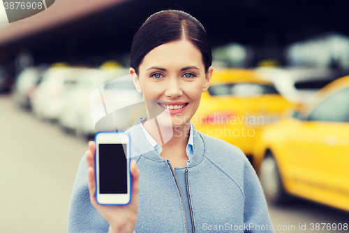 Image of smiling woman showing smartphone over taxi in city