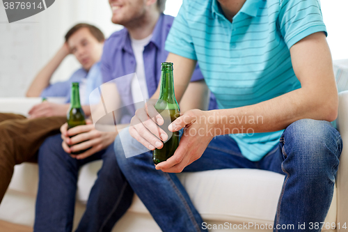 Image of happy male friends drinking beer at home