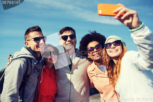 Image of smiling friends taking selfie with smartphone