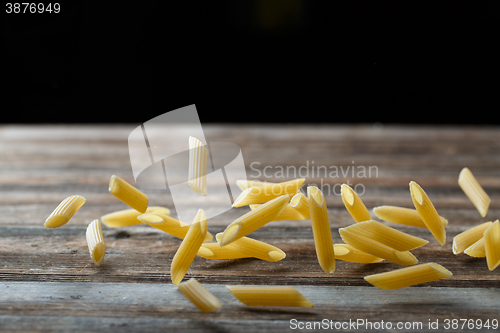 Image of Falling penne pasta. Flying yellow raw macaroni over black background.