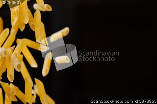 Image of Falling penne pasta. Flying yellow raw macaroni over black background.
