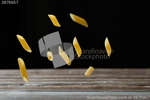 Image of Falling penne pasta. Flying yellow raw macaroni over black background.