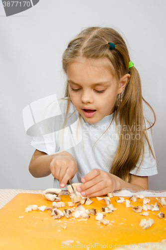 Image of The little girl at the table with diligence knife cutting mushrooms