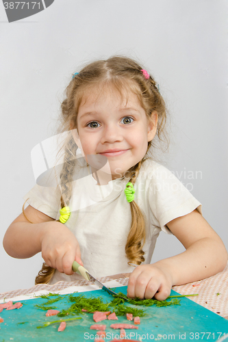 Image of Little six year old girl trying to cut the greens at the kitchen table