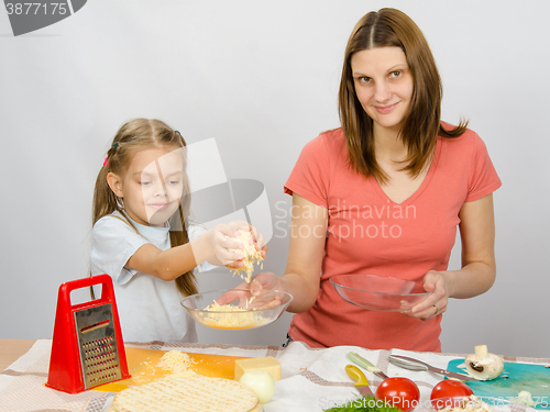 Image of  Six-year girl helps mother to rub grated cheese on pizza