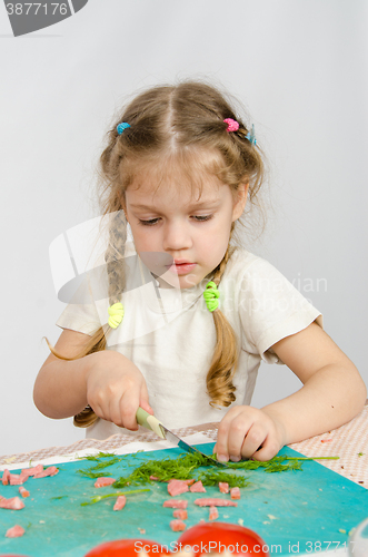 Image of Little six year old girl intently trying to cut with a knife green kitchen table