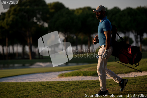 Image of golfer  walking and carrying golf  bag at beautiful sunset