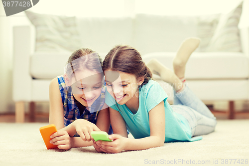 Image of happy girls with smartphones lying on floor
