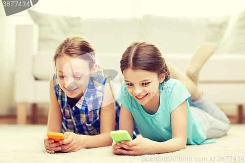 Image of happy girls with smartphones lying on floor