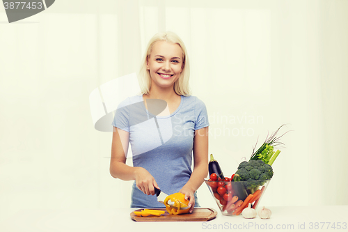 Image of smiling young woman chopping vegetables at home