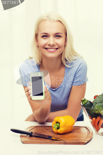 Image of smiling woman with smartphone cooking vegetables