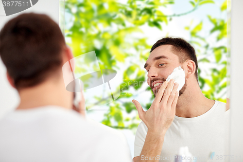 Image of happy man applying shaving foam at bathroom mirror