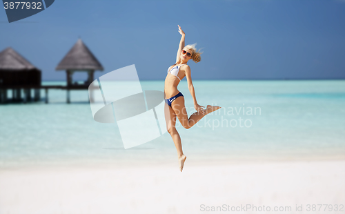 Image of happy young woman jumping over exotic beach