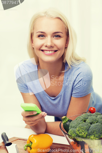 Image of smiling woman with smartphone cooking vegetables