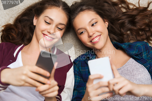 Image of happy teenage girls lying on floor with smartphone