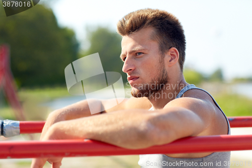 Image of young man exercising on parallel bars outdoors