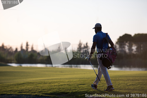 Image of golfer  walking and carrying golf  bag at beautiful sunset