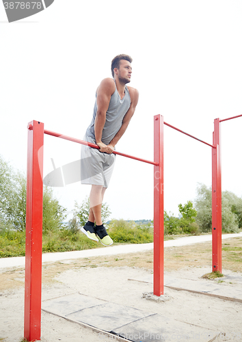 Image of young man exercising on horizontal bar outdoors