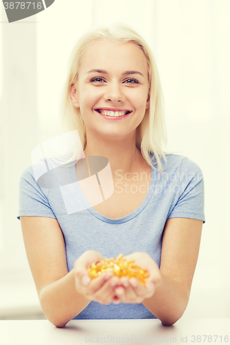 Image of happy woman holding fish oil capsules at home