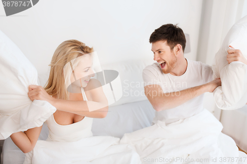 Image of happy couple having pillow fight in bed at home