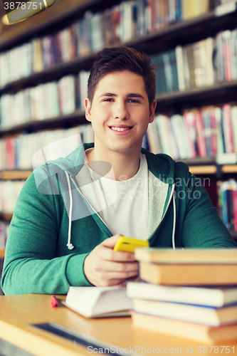 Image of male student with smartphone and books in library