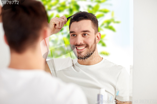 Image of happy man brushing hair with comb at bathroom