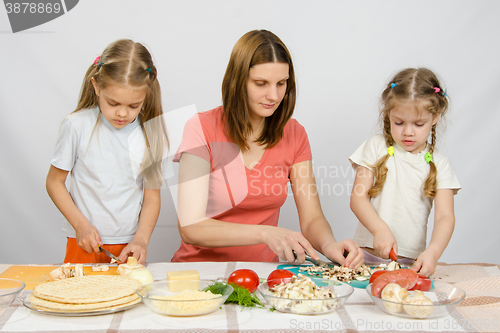 Image of Mom teaches two daughters to cook. It helps them to cut mushrooms and vegetables