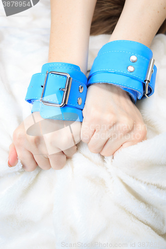 Image of female hands in leather handcuffs. on the background sheet. sex toys.