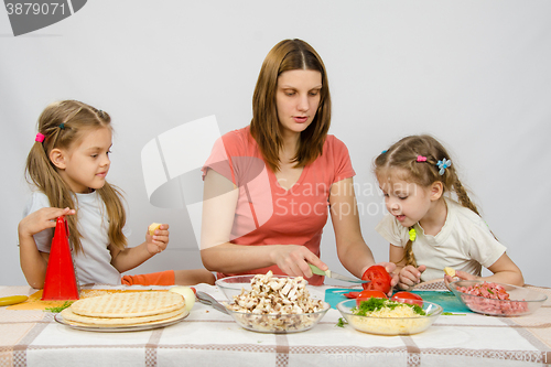 Image of Mom shows two young daughters at the kitchen table as the cut tomato pizza