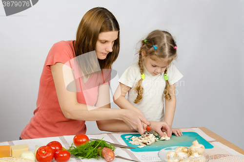 Image of Mom shows daughter how to cut a small knife mushrooms