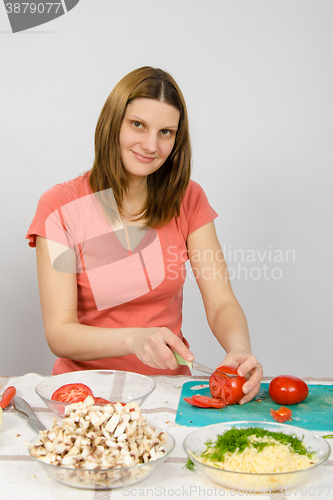Image of The girl at the kitchen table cutting the tomato